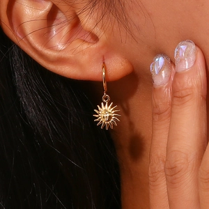 Golden stainless steel hoop earrings with vintage sun face pendant worn by model