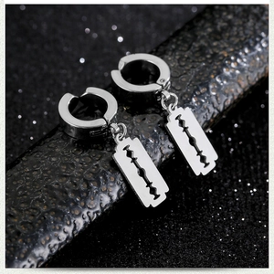 Macro view of stainless steel hoop earrings with a razor blade pendant on a black base