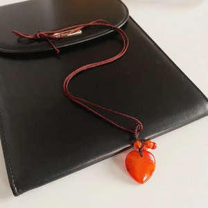 Detail of red agate heart pendant with woven cord on black leather jewelry pouch