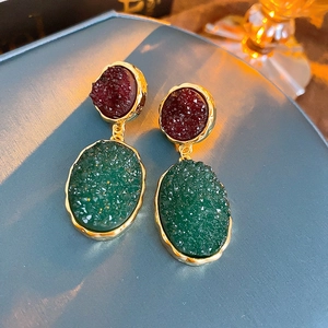 Macro detail of vintage gold earrings with deep red and green textured resin stones