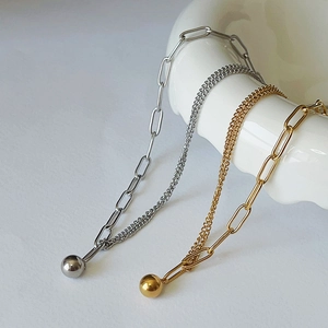 Detail of asymmetric gold and silver chain bracelets with a spherical metal pendant charm