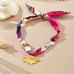 Vue détaillée du collier en ruban de soie rose avec pendentif tournesol doré sur le sable