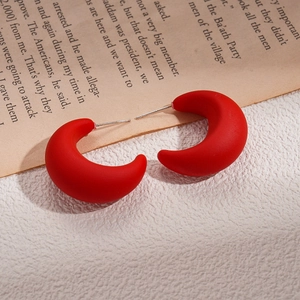 Matte red crescent C-shaped acrylic earrings displayed on a vintage newspaper background