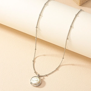 Collier minimaliste à chaîne argentée avec pendentif perle ronde sur fond beige