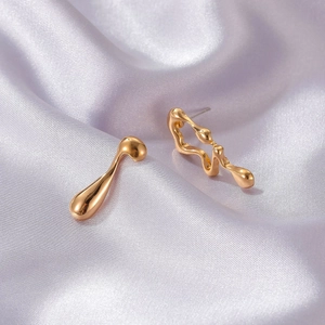 Macro shot of liquid metal style gold asymmetric earrings on a silk fabric background