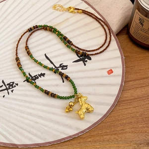 Detail of tiger eye stone necklace with gold-plated horse pendant on a vintage fan