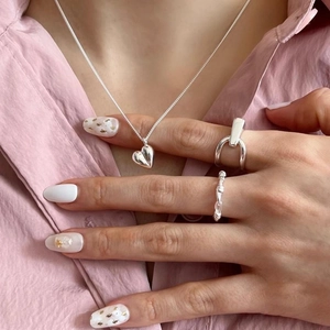 Close-up of woven sterling silver rings and heart pendant necklace on model with pink shirt