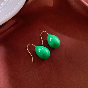 Detail view of glossy green water drop earrings on elegant dark red silk background
