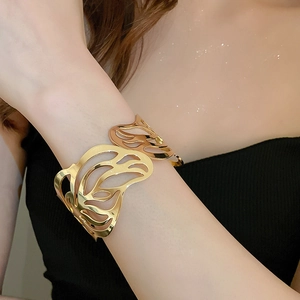 Detail of wide open gold cuff bracelet with hollow leaf patterns on female arm