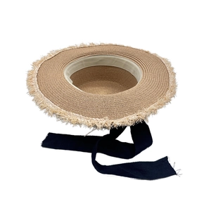 Detailed macro view of wide brim straw sun hat featuring fringe edges and black ribbon tie