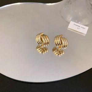 Detailed view of glossy gold intertwined spiral earrings reflecting on a mirror surface