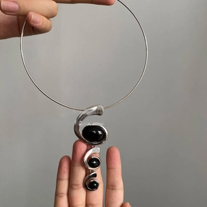 Detail of silver collar with three black resin pendants in irregular spiral metal frames