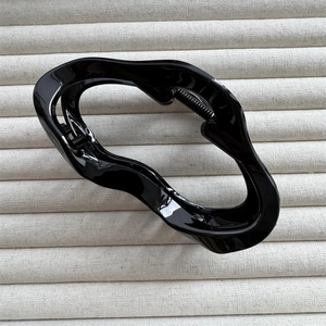 Close-up of black wave-shaped hair claw clip on beige striped fabric background
