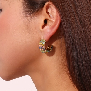 Close-up of golden C-shaped earring with colorful rhinestones on a model's ear