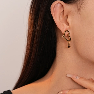 Detailed close-up of heart-shaped gold earrings with black zircon stones and saturn pendant