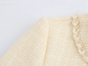 Detailed macro view of beige tweed fabric texture and gold braided edge on the dress