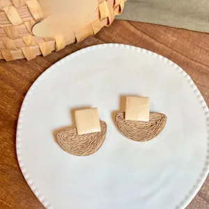 Detail of bohemian raffia drop earrings with wooden studs on a white ceramic tray