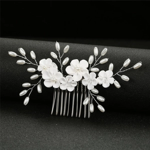 White clay flower and pearl bridal hair comb accessory on a textured black stand