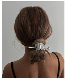 Detail of irregular silver metal hair pin with a single pearl in a messy low bun hairstyle