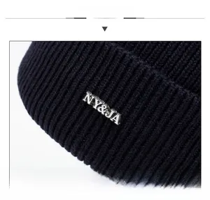 Détail du bonnet en maille côtelée noire avec logo métallique NY&JA de style urbain