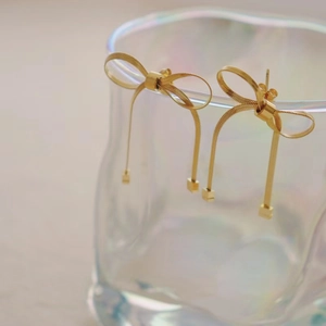 Close-up of golden bow earrings with long chain tassels hanging on a glass cup