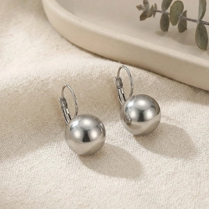 Detailed close-up of silver stainless steel ball drop earrings on textured beige fabric