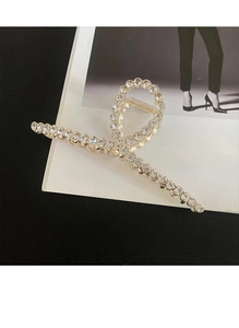 Grosse pince à cheveux en métal doré ornée de strass brillants posée sur un magazine chic