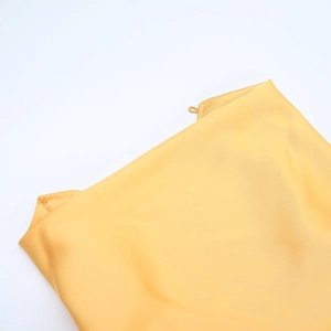 Gros plan sur les coutures fines et la texture satinée brillante de la robe jaune dos nu