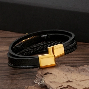 Detail of woven black leather bracelet with a polished gold magnetic metal clasp on stone