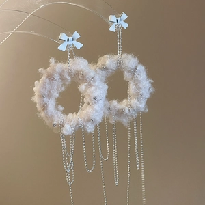 Detail view of white plush round earrings with silver chain tassels and bow accent