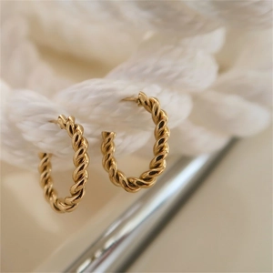 Macro shot of gold C-shaped twisted hoop earrings hanging on a white textured rope
