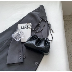 Flat lay of a black pleated dumpling chain bag styled on a grey blazer and lifestyle magazine