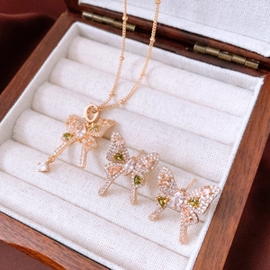 Detailed view of vintage gold bow jewelry set with green and white zircons on velvet stand