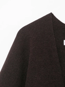 Close-up detail of dark brown knit poncho texture and shoulder seam on white background