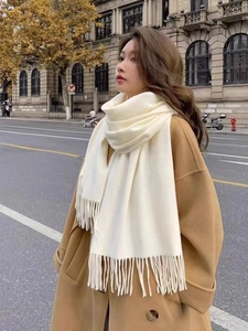 Close-up of cream faux cashmere scarf with long tassels paired with a camel coat