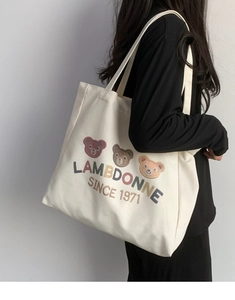 Detail of embroidered teddy bears on a beige canvas tote bag worn by a model
