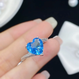 Primer plano de anillo con gema azul en forma de corazón y diamantes en banda de plata