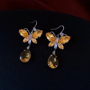 Detail of butterfly zircon earrings with yellow teardrop pendants on a dark surface
