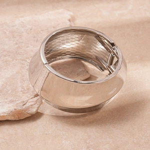 Polished silver metal wide cuff bracelet with a spring hinge mechanism on a natural stone