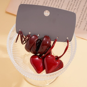 Set of three deep red geometric hoop and heart drop earrings in a decorative glass bowl