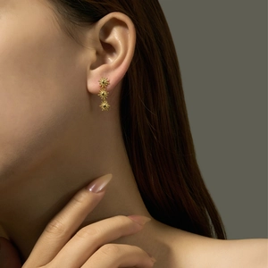 Close-up of a model wearing three linked gold sunburst dangle earrings in sterling silver