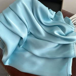 Elegant light blue satin silk scarf with soft luster draped on a leather surface
