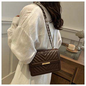 Detail of dark brown quilted crossbody bag with V-shaped stitching and gold chain strap