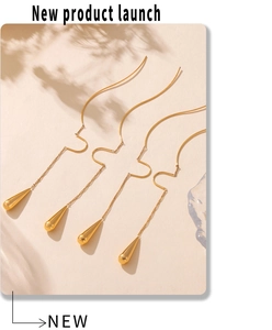 Detail of elegant gold tassel earrings with teardrop pendants on sand texture background