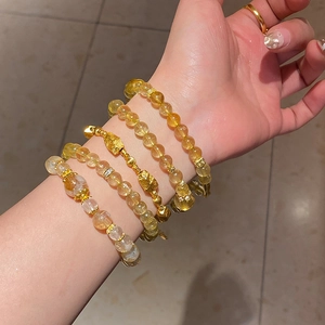 Detail of stacked citrine beaded bracelets with gold charms and zircon flower accents