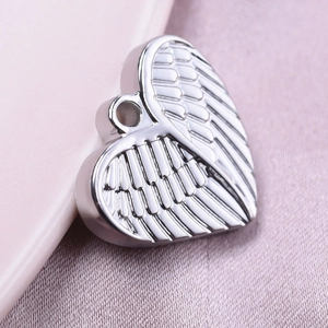 Macro shot of silver heart pendant with wing texture on soft pink fabric background