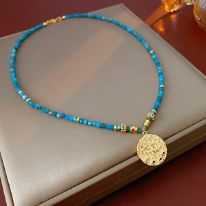 Detail of blue beaded necklace featuring a golden evil eye pendant with crystal inlay