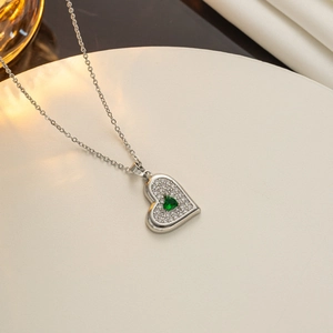 Detailed view of silver heart pendant with green emerald zircon on a beige display stand