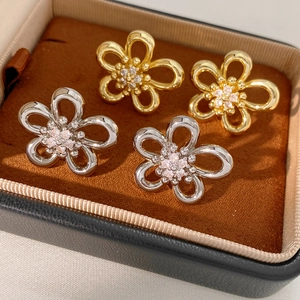 Macro detail of hollow flower stud earrings with zircon centers in gold and silver finish