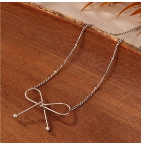Close-up of a silver bow necklace with bead chain on a rustic dark wood surface